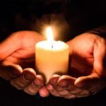 Mãos segurando vela acesa lembrando fé em Deus